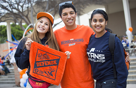 3 CSUF students smiling during Homecoming event with spirit gear