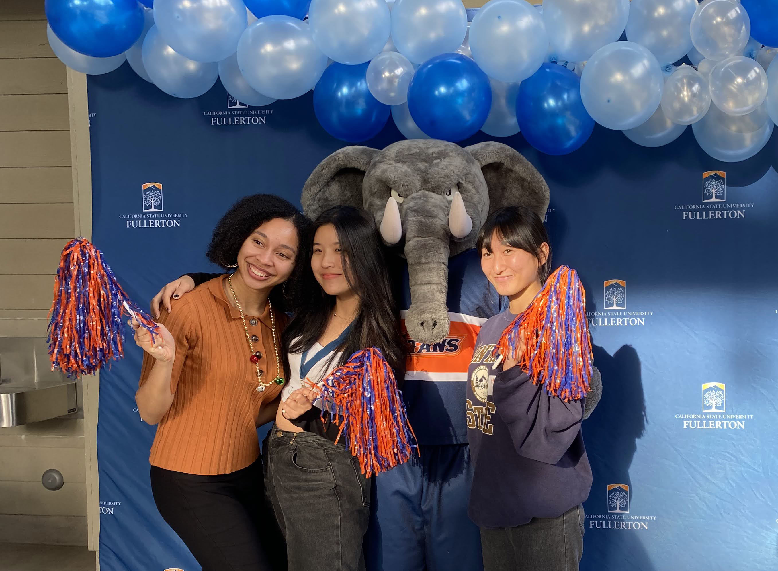 3 students posing in front of photo backdrop with Tuffy the Titan